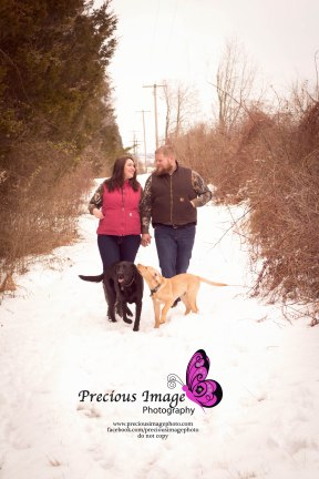 couple holding hands and walking dogs in the snowy woods engagement session